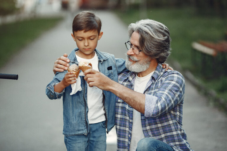 Grandfather walking in the park with his grandson, enjoying an ice cream